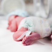 Newborn baby boy covered in vertix inside incubator